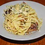 Parma ham fig and blue cheese spaghetti In a white bowl on a wooden table