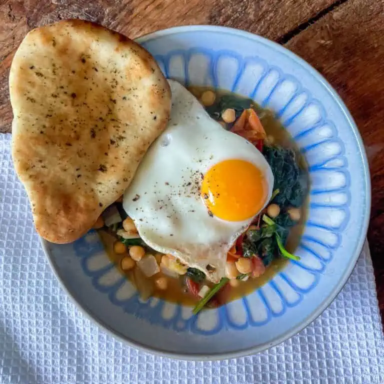 spinach and chickpea curry with fried egg top view with garlic naan