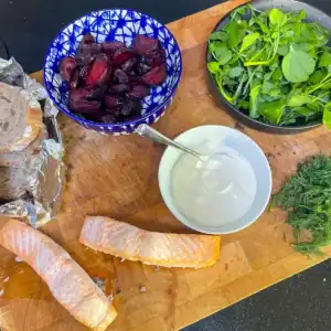 Top-down view of salmon and beetroot sharer with sliced roasted beetroot, flaky salmon, soured cream, watercress, dill, and rye bread ready for serving.