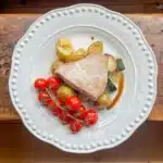 pan fried tuna on top of potatoes and courgettes with tomatoes on a white plate