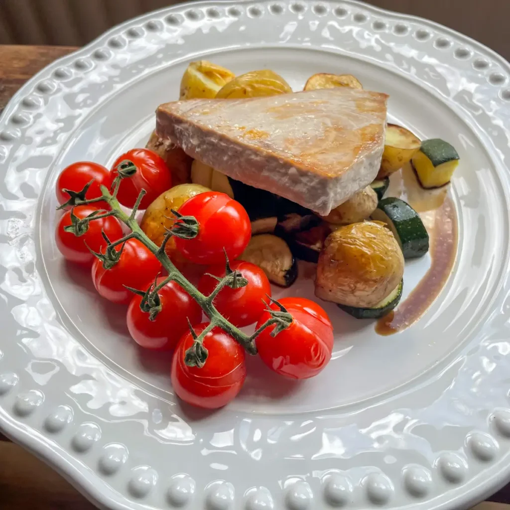 Seared tuna and roasted potatoes, courgettes and tomatoes on a white plate
