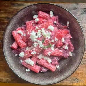 Pink Beetroot and feta pasta in a black bowl on a wooden table
