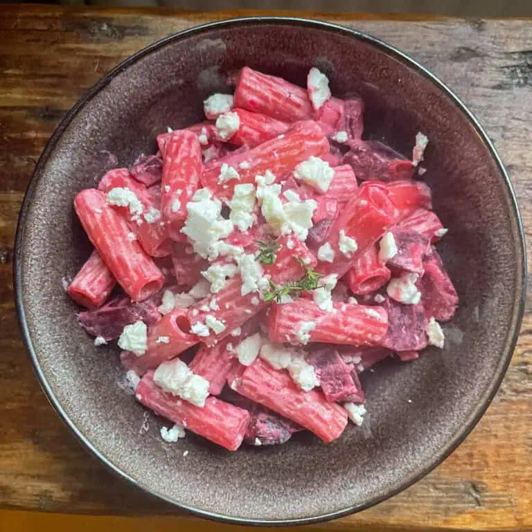 Pink Beetroot and feta pasta in a black bowl on a wooden table