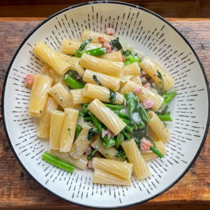 Top view of creamy pancetta broccoli and dolcelatte pasta in a white bowl on a wooden table
