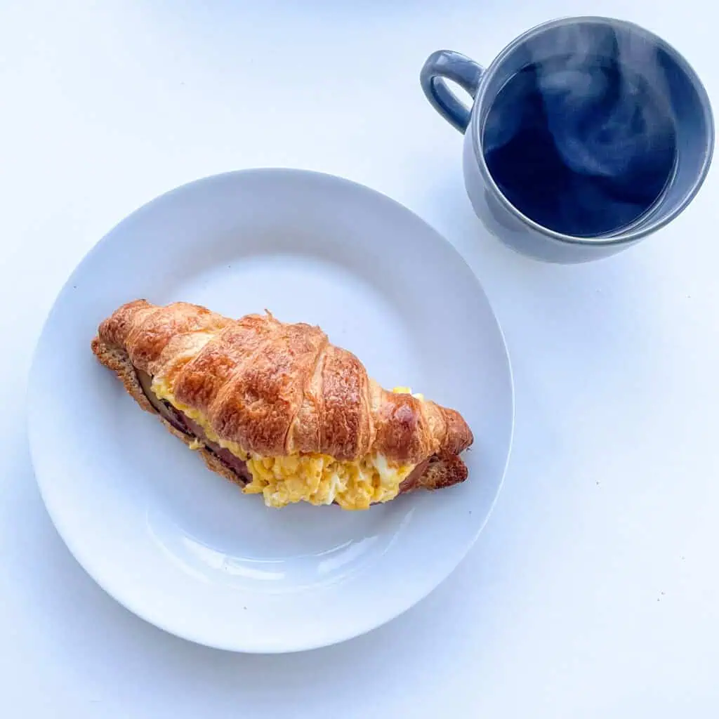 Stuffed croissant sandwich on a white plate with a black coffee on the side