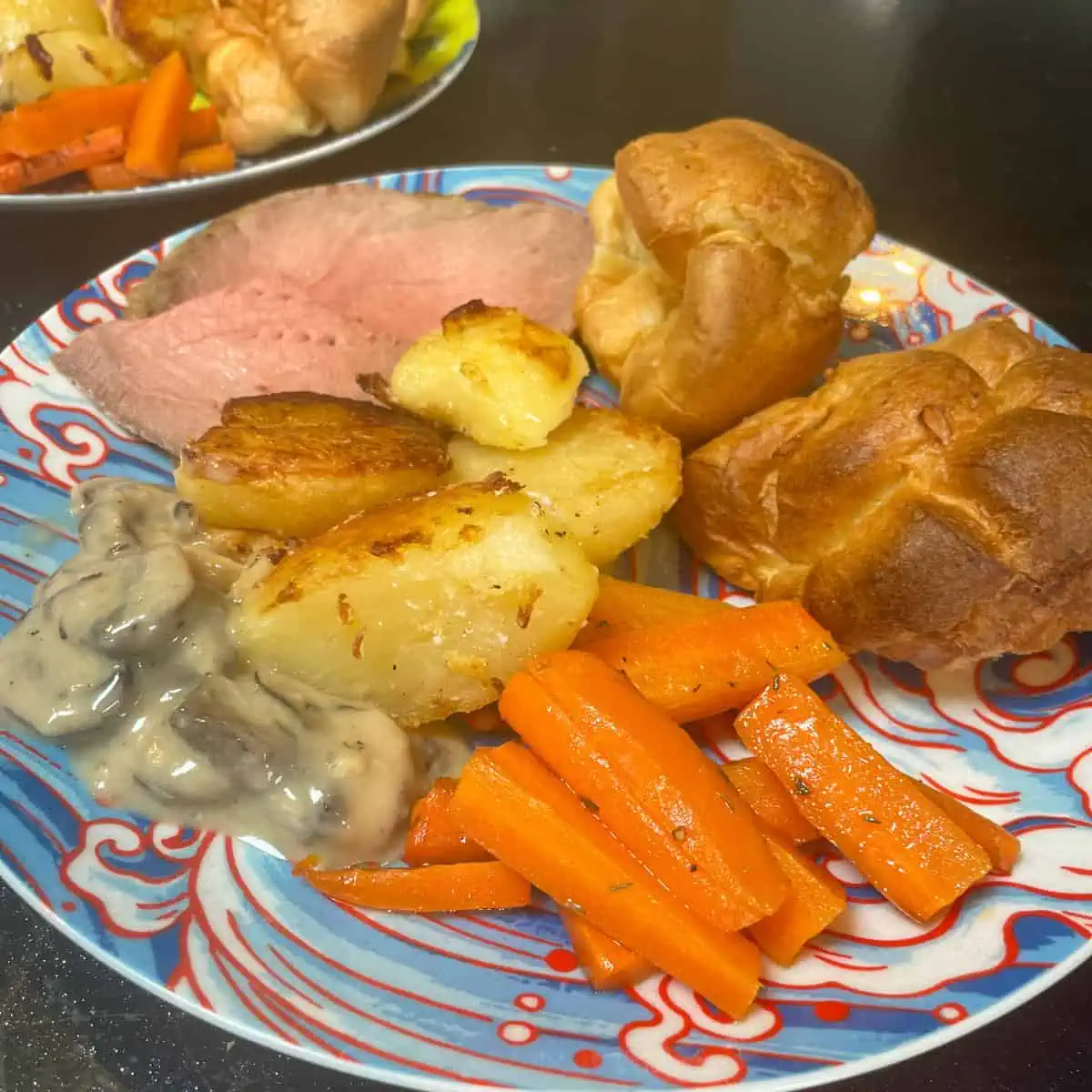 A plate full of roast dinner with roast beef, roast potatoes, Yorkshire puddings and honey roast carrots