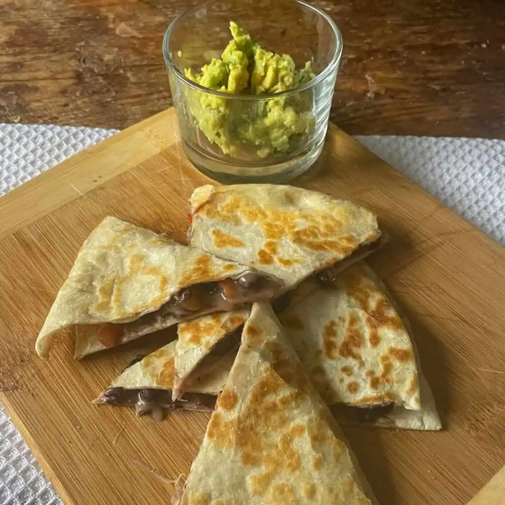 Black bean quesadillas on a wooden board with a minty avocado dip