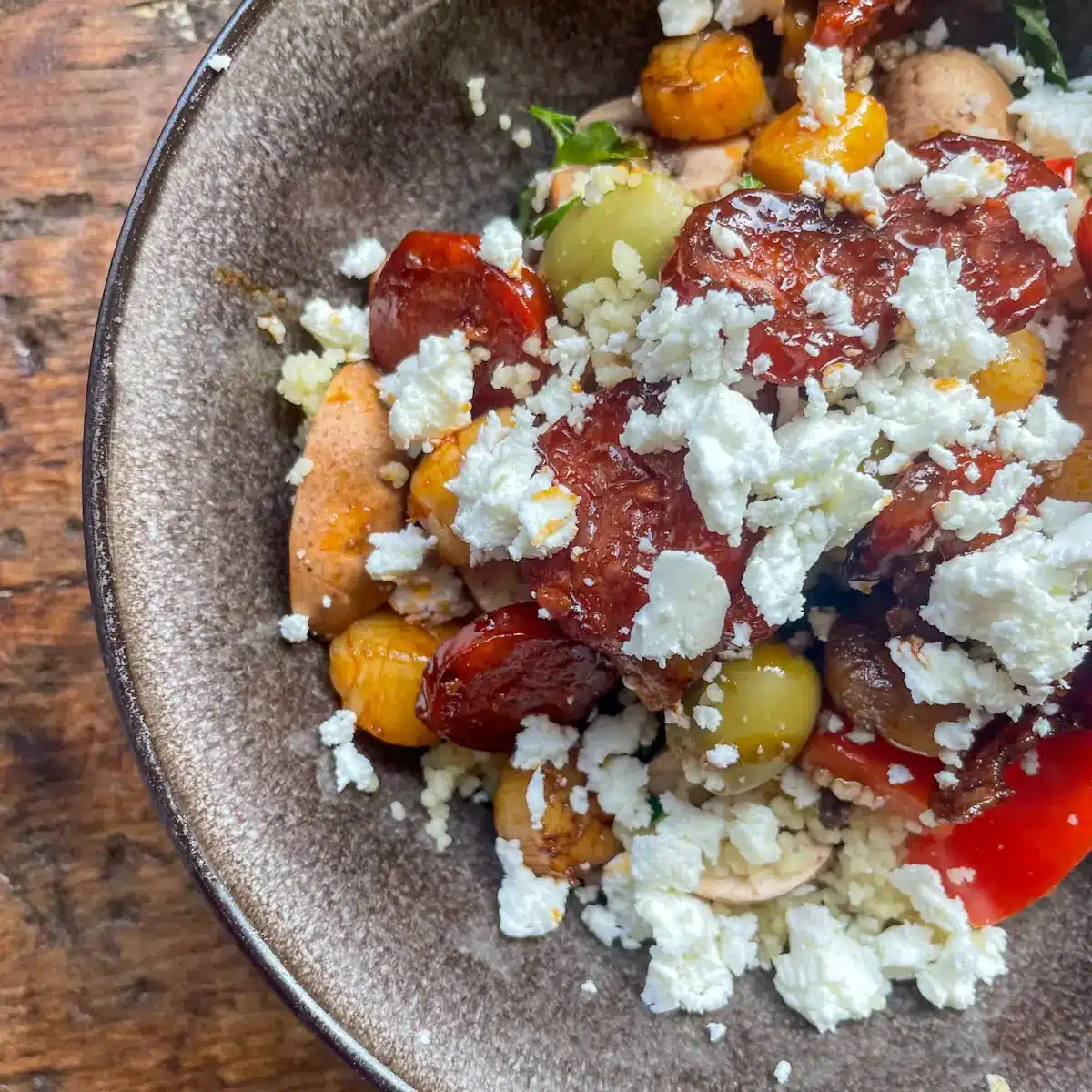 Vegetable couscous topped with glazed chorizo and scallops and crumbled feta