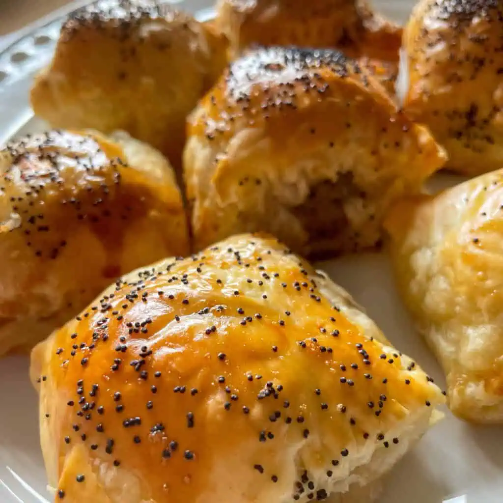 Flaky golden smoked cheese sausage rolls on a white plate