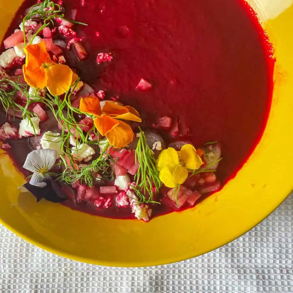Chilled beetroot soup in a bowl topped with feta and edible flowers