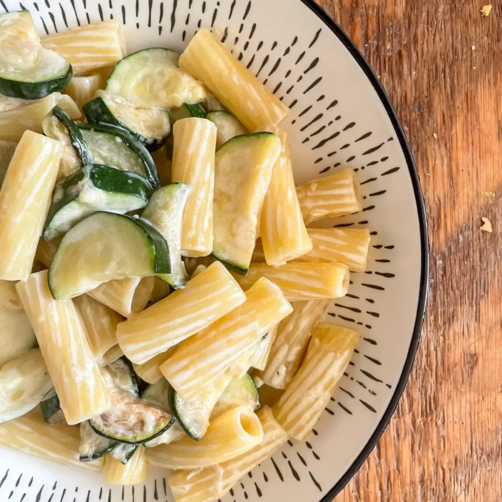 Creamy courgette pasta close up in a white bowl on a wooden table