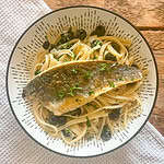 Pan fried sea bass with black olive linguine In a white bowl on a wooden table