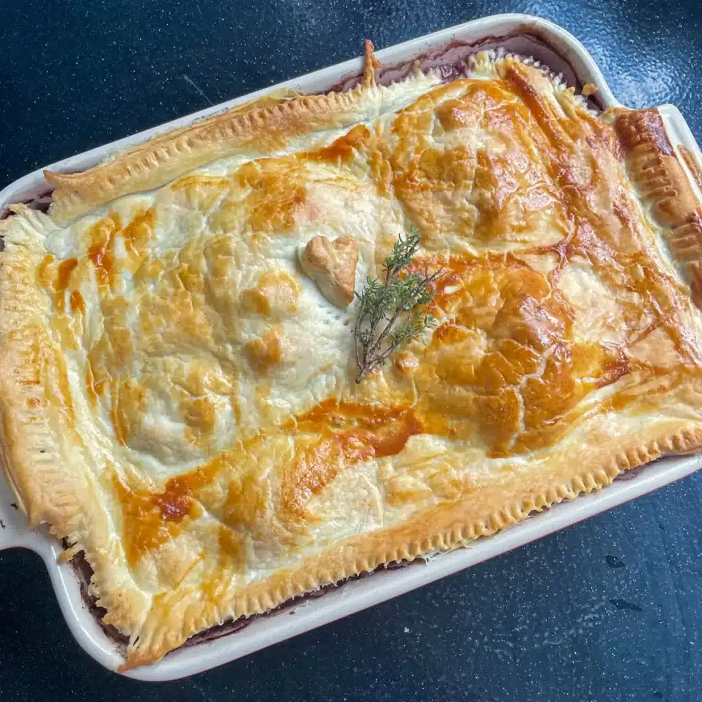 overhead shot of coq au vin pie topped with puff pastry and a sprig of thyme