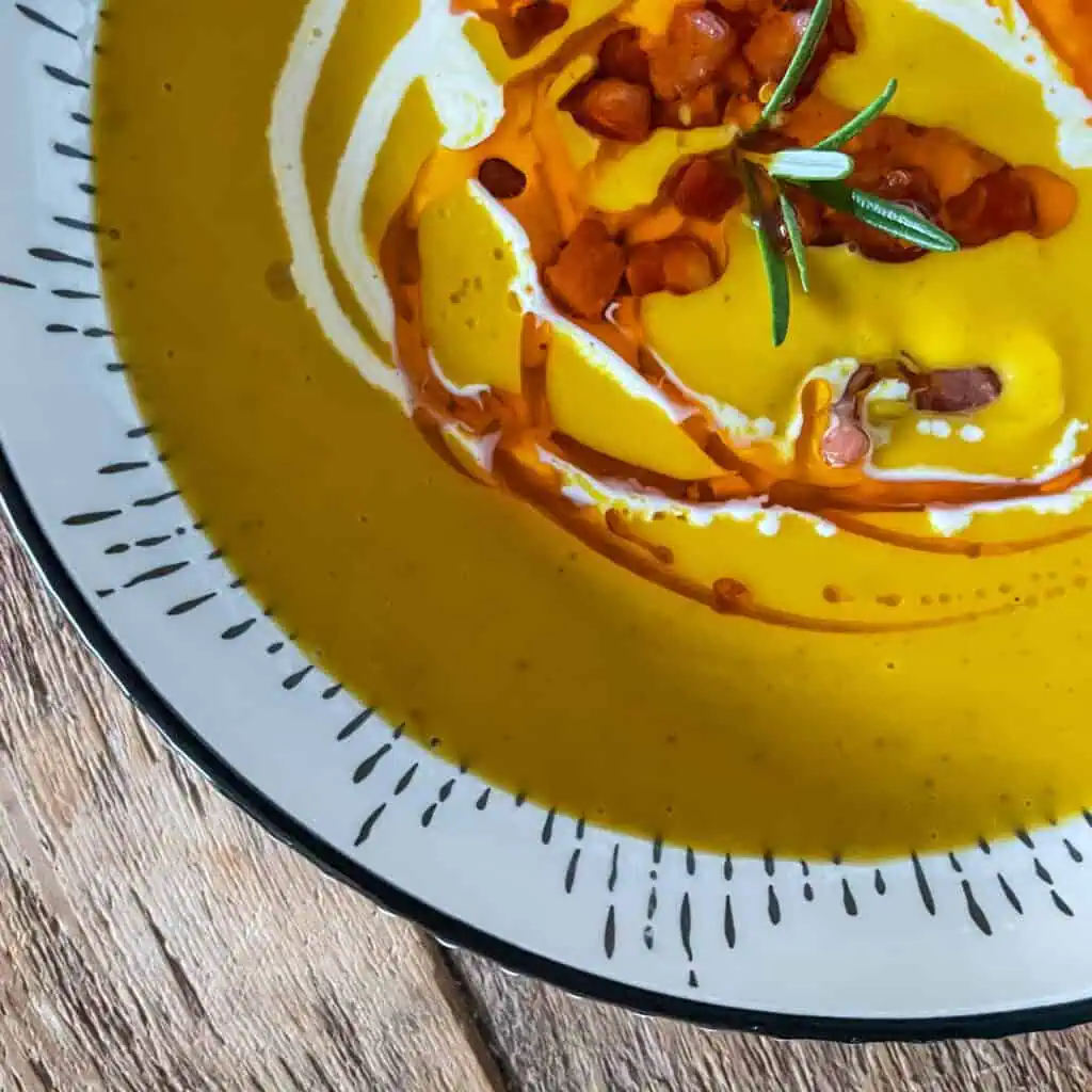Roasted butternut squash soup with cream swirl and chilli oil in a white bowl