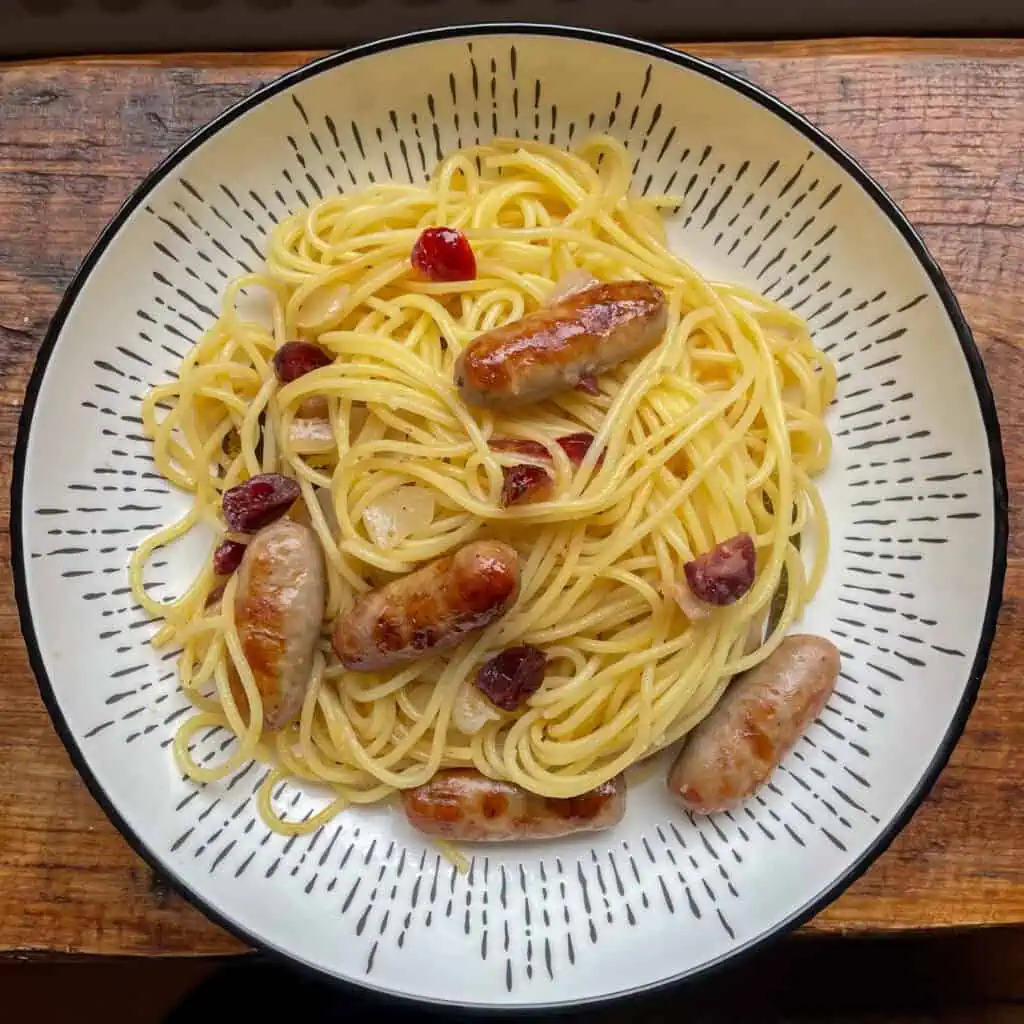 Sausage and cranberry pasta In a white and black bowl on a wooden surface
