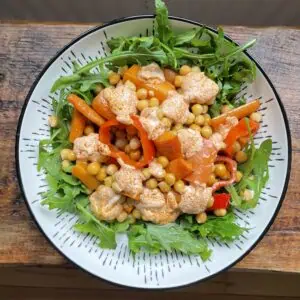 Warm roasted chickpea salad With dressing in a white bowl on a wooden table
