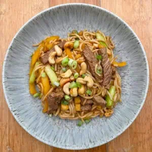Kung pao stir fry beef with noodles In a blue bowl on a wooden table