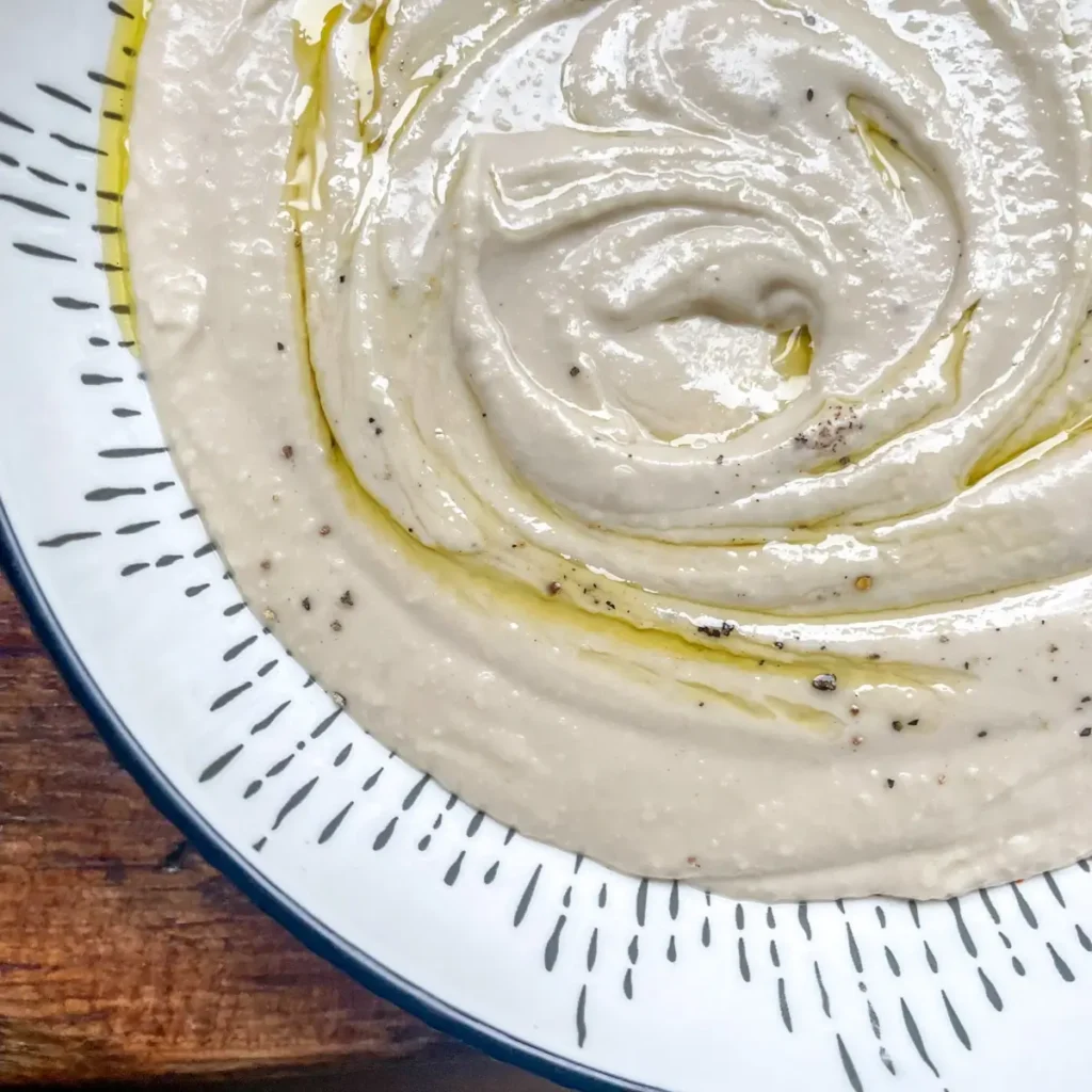 Close up of white bean hummus in a bowl drizzled with olive oil