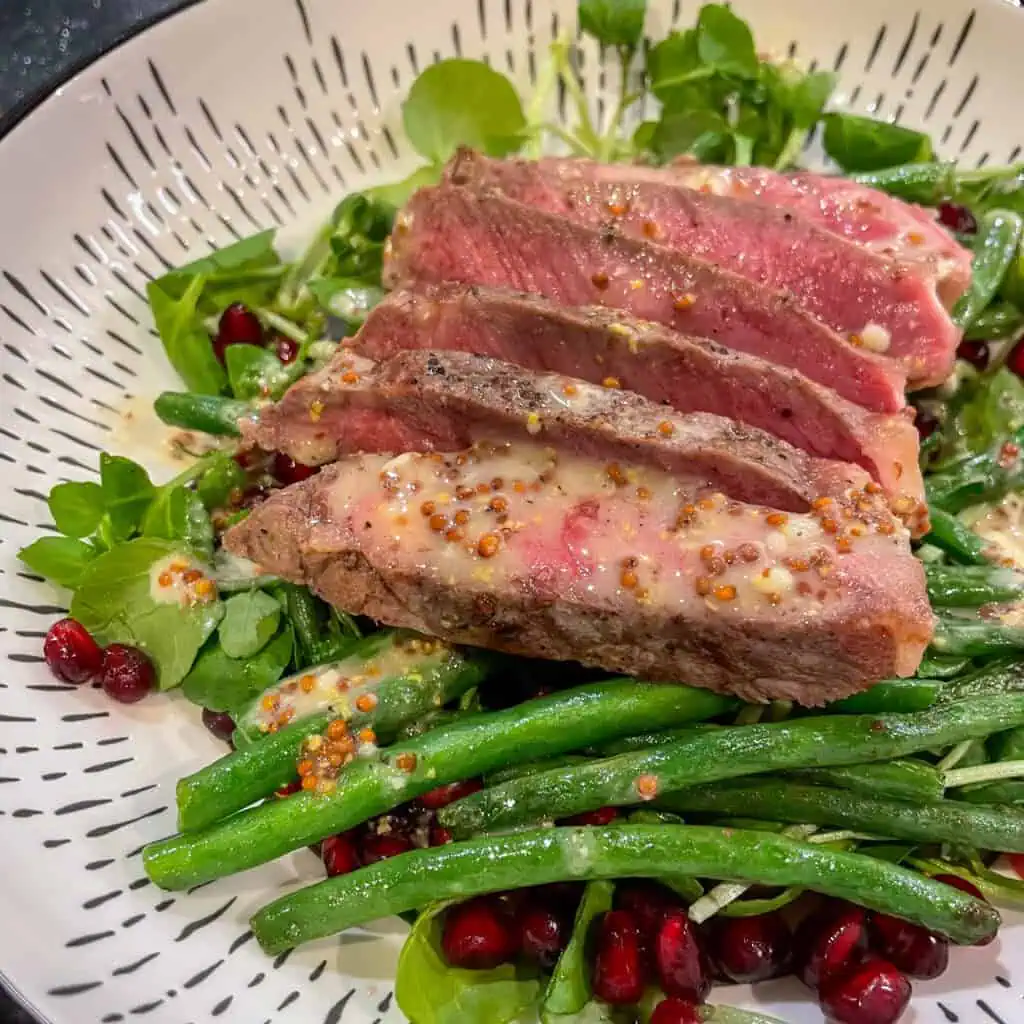 A steak and green bean salad with mustard dressing in a white bowl