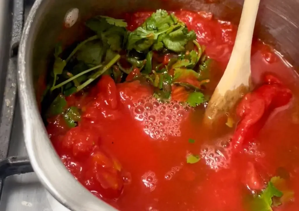 Adding tomatoes and coriander to the soup and simmering