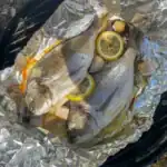 Grilled whole sea bream on the barbecue stuffed with lemon, garlic, and dill – simple summer fish recipe idea.