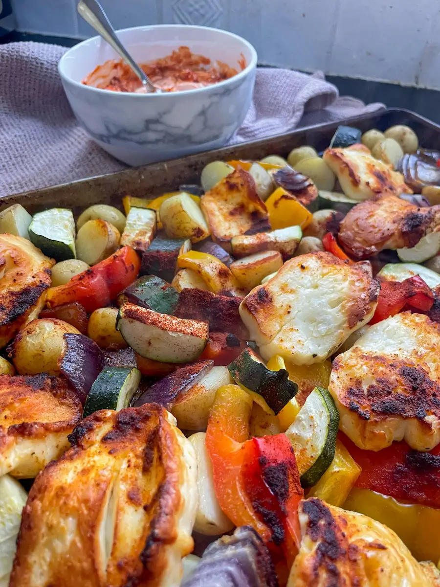 Halloumi traybake with courgettes, potatoes, peppers and red onion with harissa yoghurt in the background
