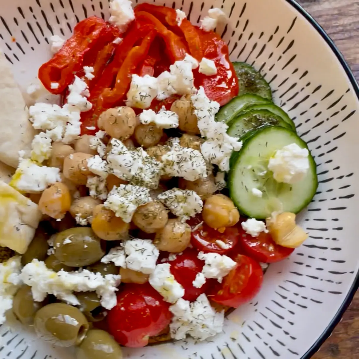 Hummus bowl topped with chickpeas tomatoes cucumber and feta