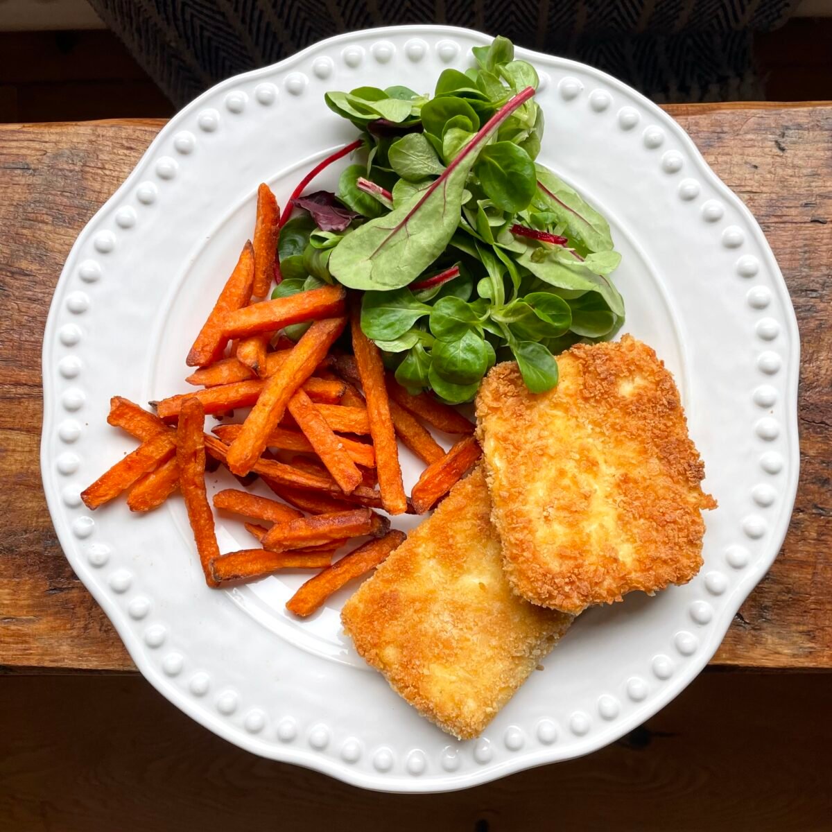 crispy fried halloumi schnitzels on a white plate with sweet potato fried and salad