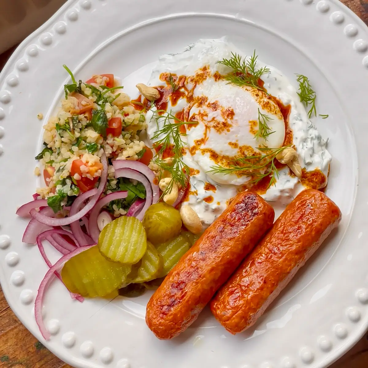 Turkish eggs on a white plate with chorizo sausages and tabbouleh