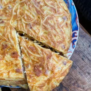 spaghetti tortilla with a slice cut out of it on a blue plate