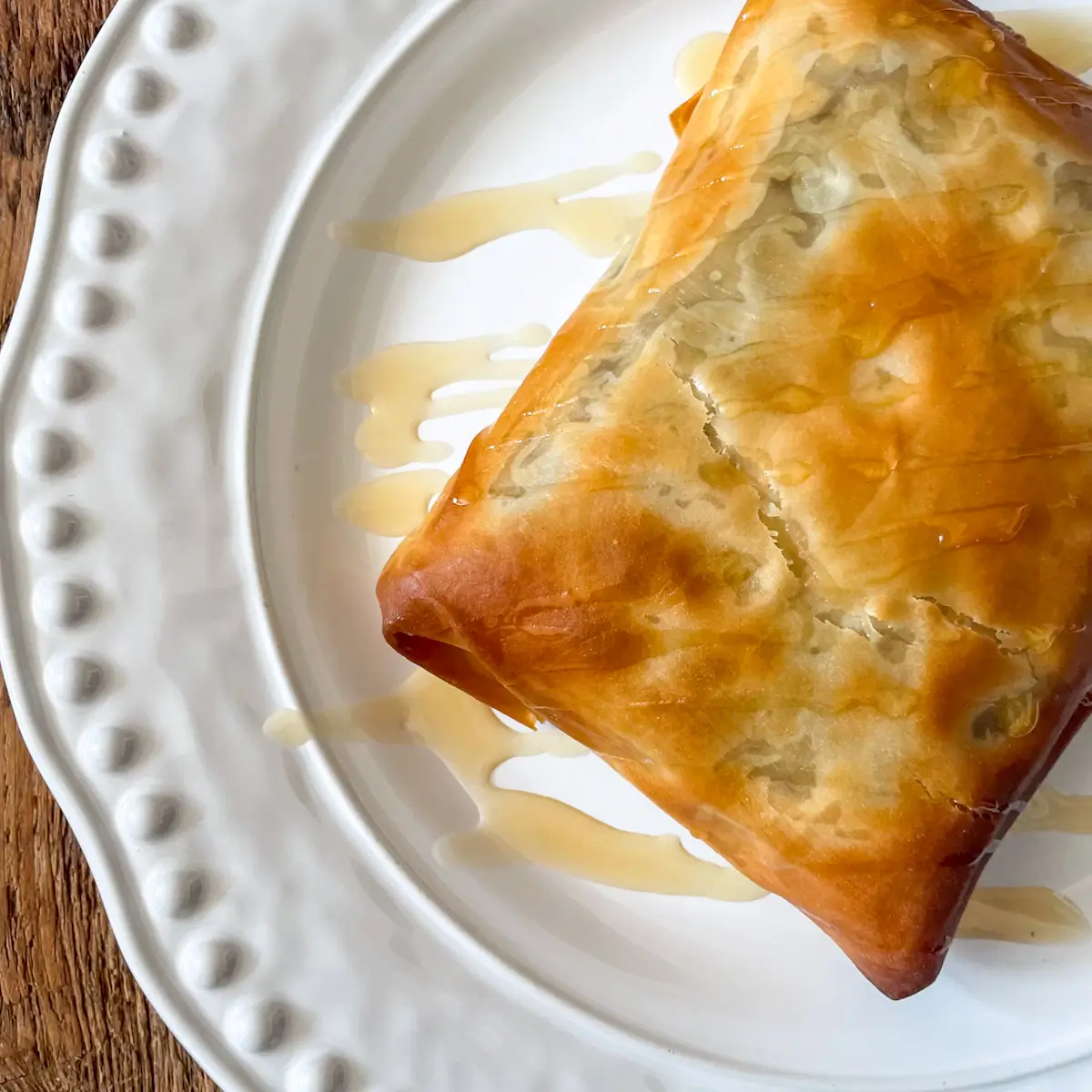 close up of a crispy filo parcel stuffed with feta and blackcurrant on a white plate