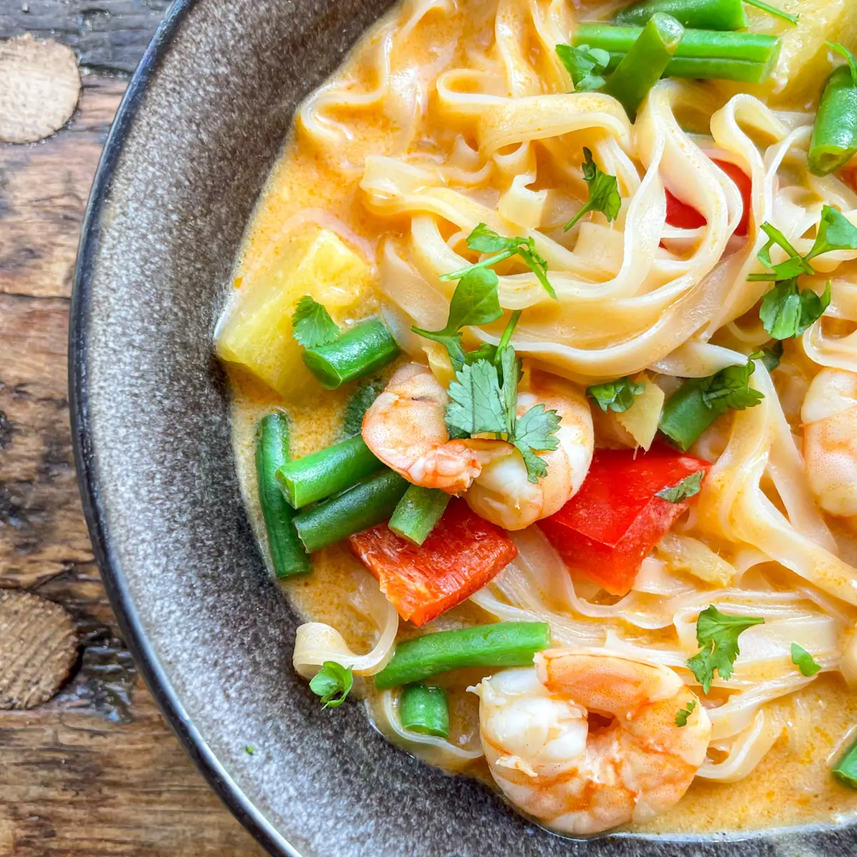 a black bowl filled with thai red prawn curry with noodles