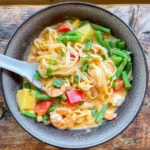 an overhead image of a thai red prawn and pineapple curry in a black bowl with a spoon