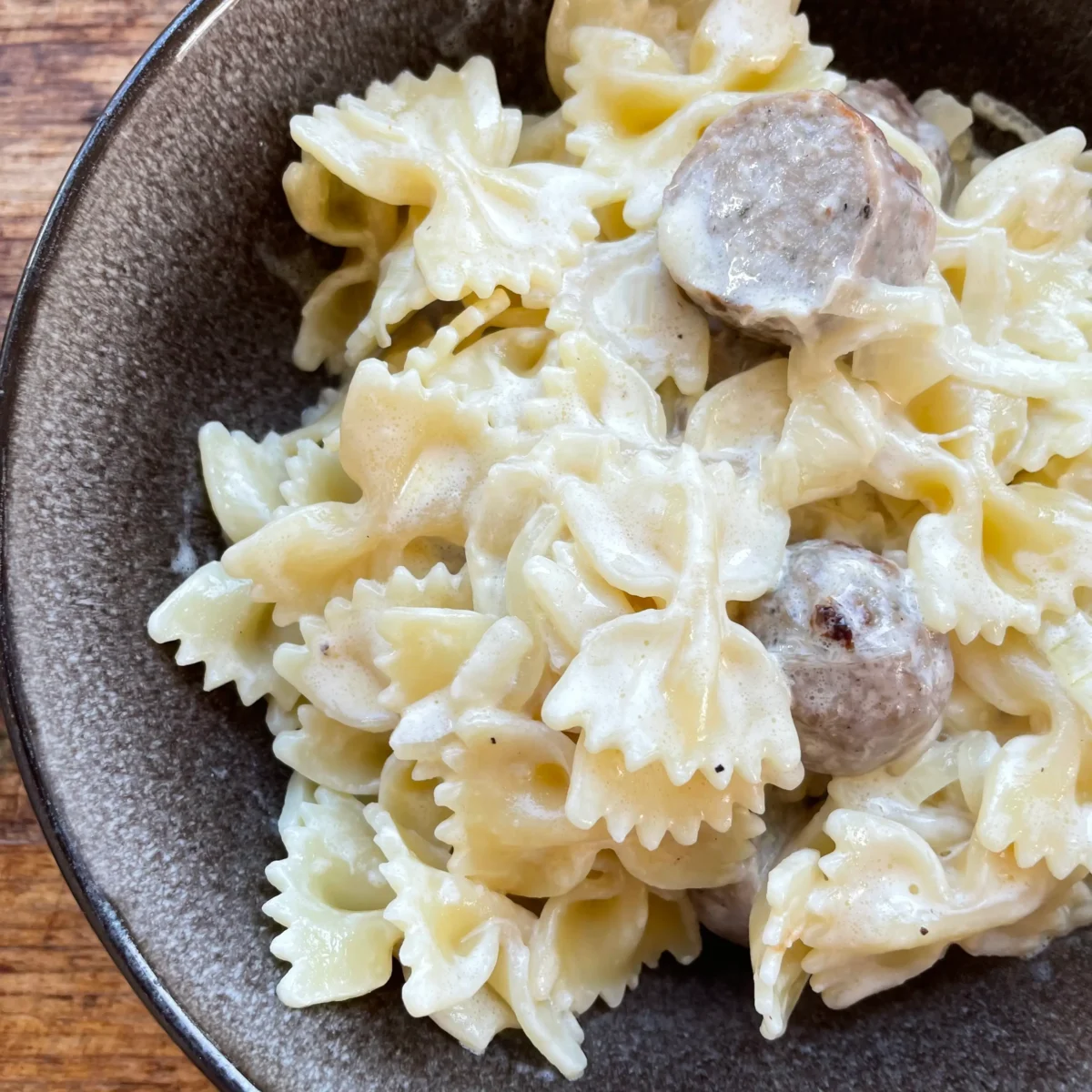 close up of caramelised onion pasta with sausages in a black bowl