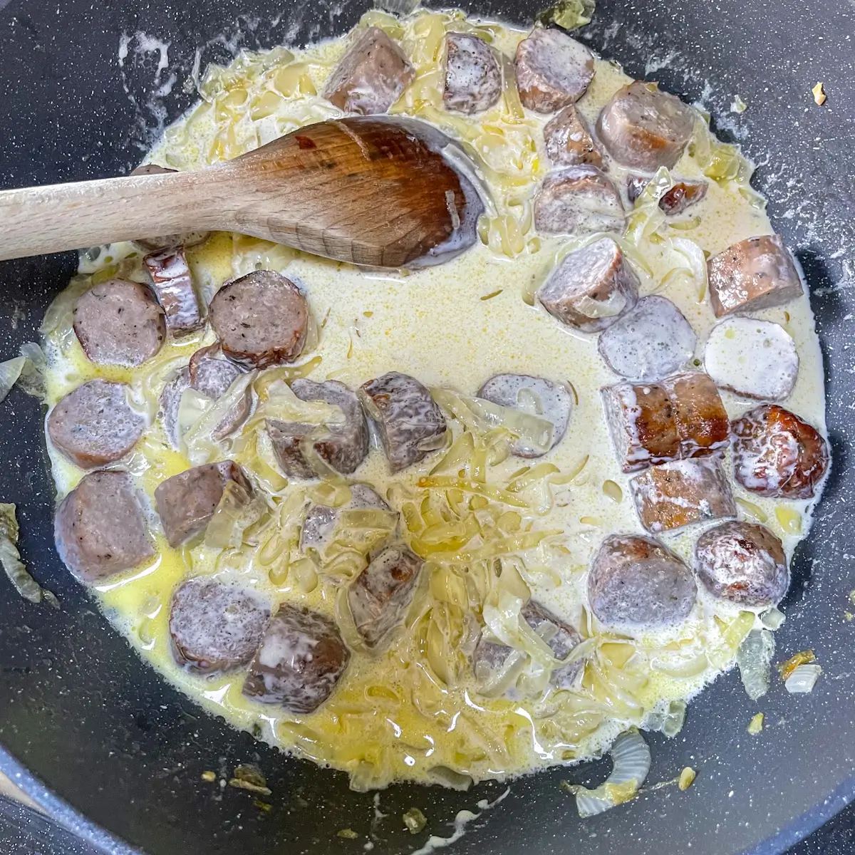 adding cream and sausages to the onions