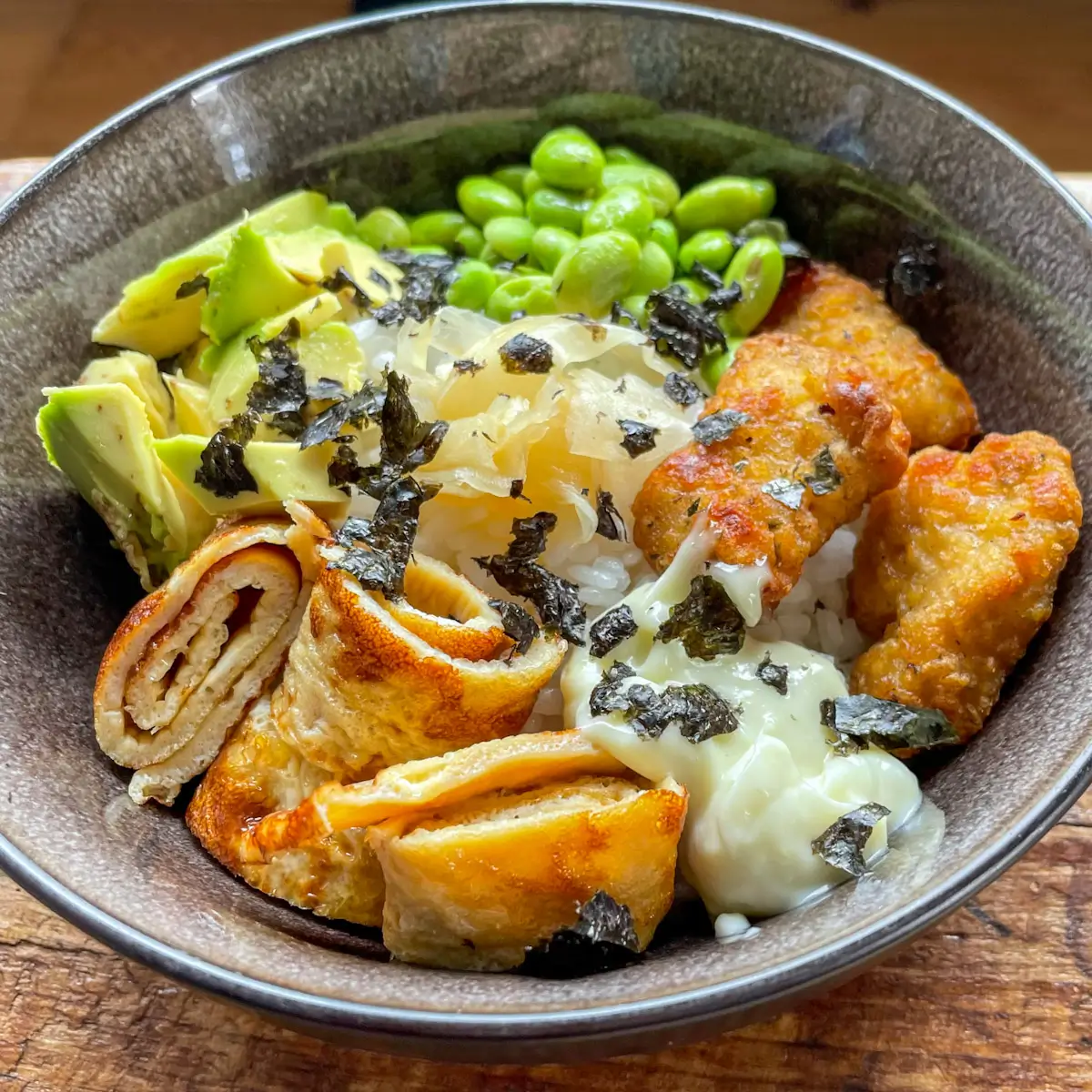 chicken nuggets, Japanese omelette and vegetables with sushi rice in a black bowl