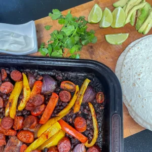 a sheet pan with chorizo and black beans ready to be served as fajitas with wraps and avocado
