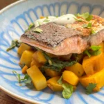 Saag aloo topped with pan fried salmon and salted yoghurt in a blue bowl