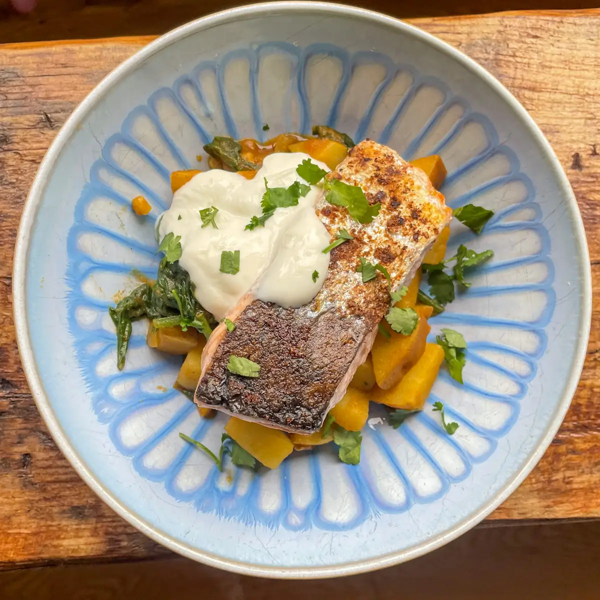 A bowl of curried potatoes and spinach topped with salmon and yoghurt