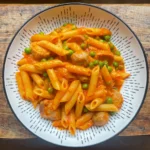overhead view of a bowl of pasta with roasted red pepper and sausage sauce in a white bowl