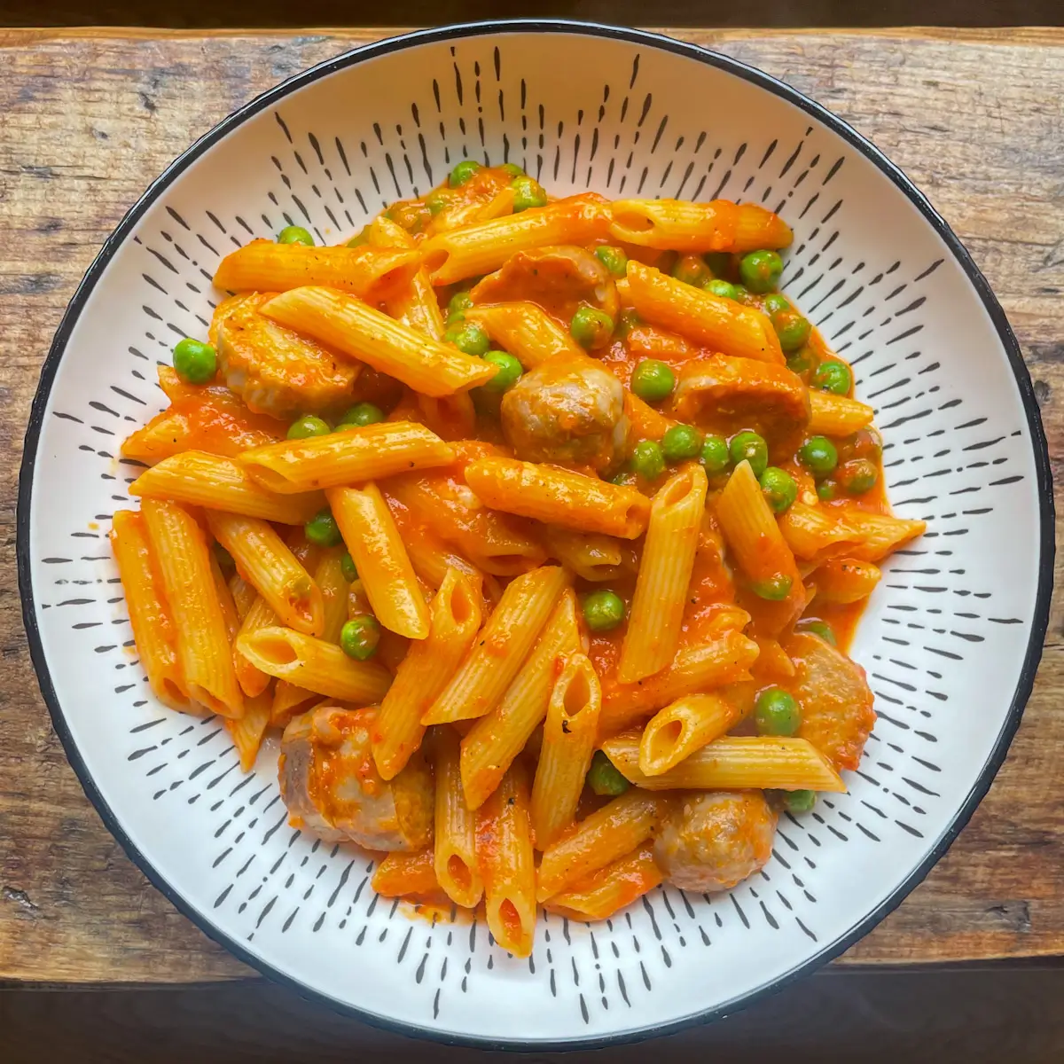 overhead view of a bowl of pasta with roasted red pepper and sausage sauce in a white bowl